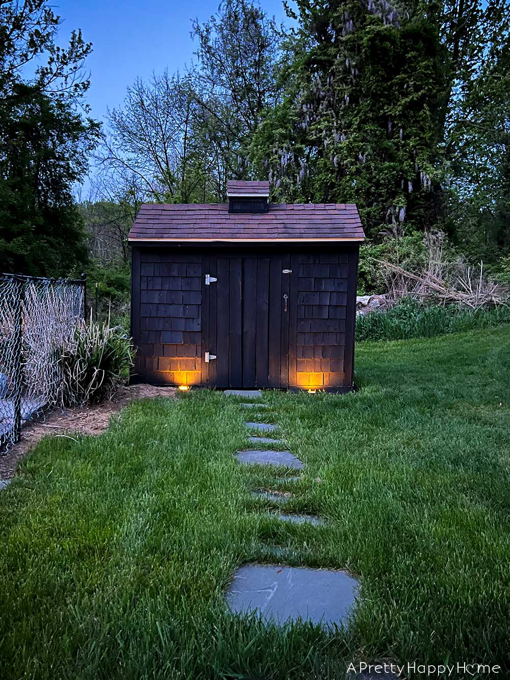 flagstone path on grass leading to pool pump house shown at night with landscaping lights