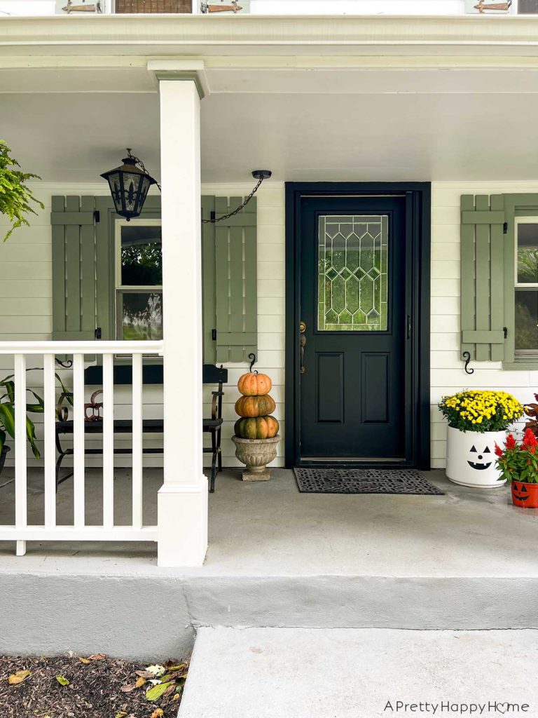 Our Fall Front Porch with pumpkin topiary in a concrete planter and a black farmhouse bench and a trio of jack o'lantern flower planters