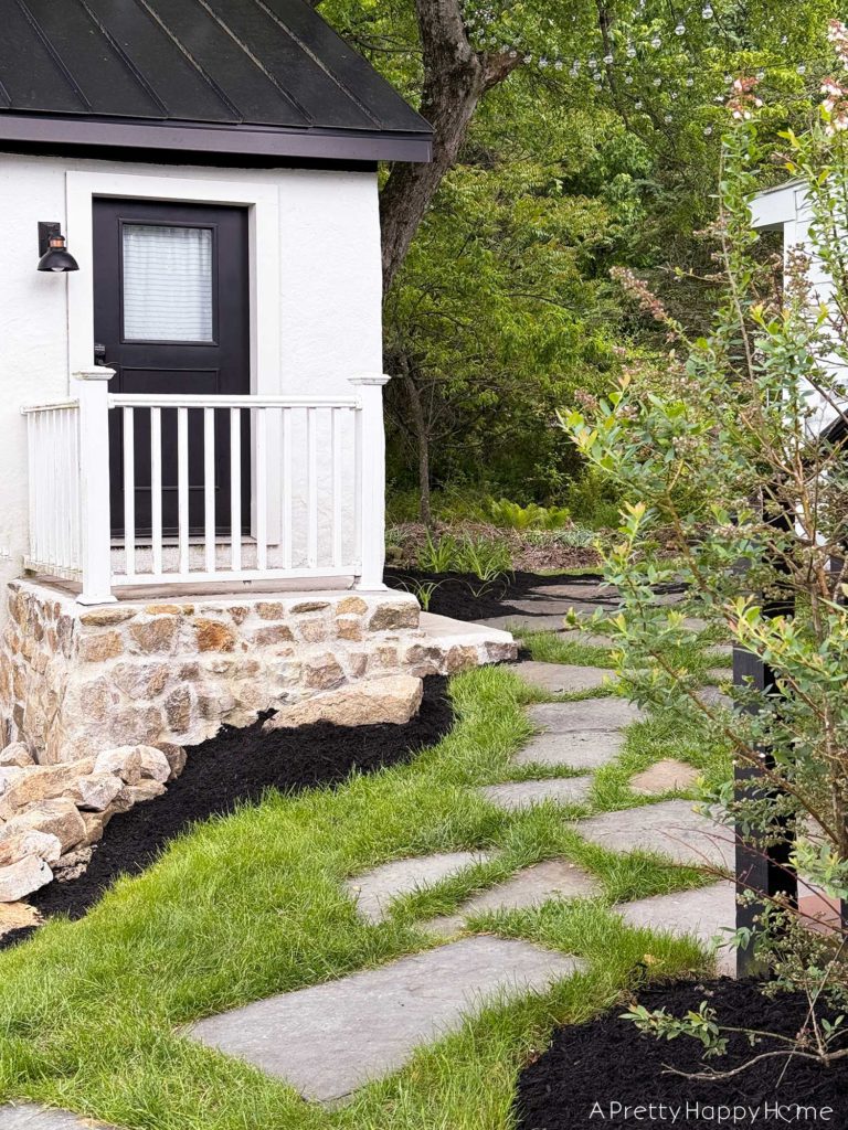 white carriage house with stone foundation and flagstone path