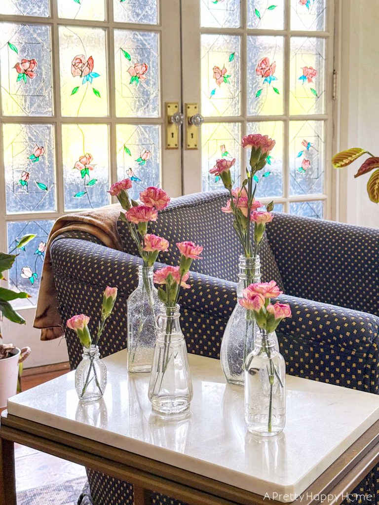 carnations in vintage bottle bud vases sitting on a marble side table in front of stained glass french doors