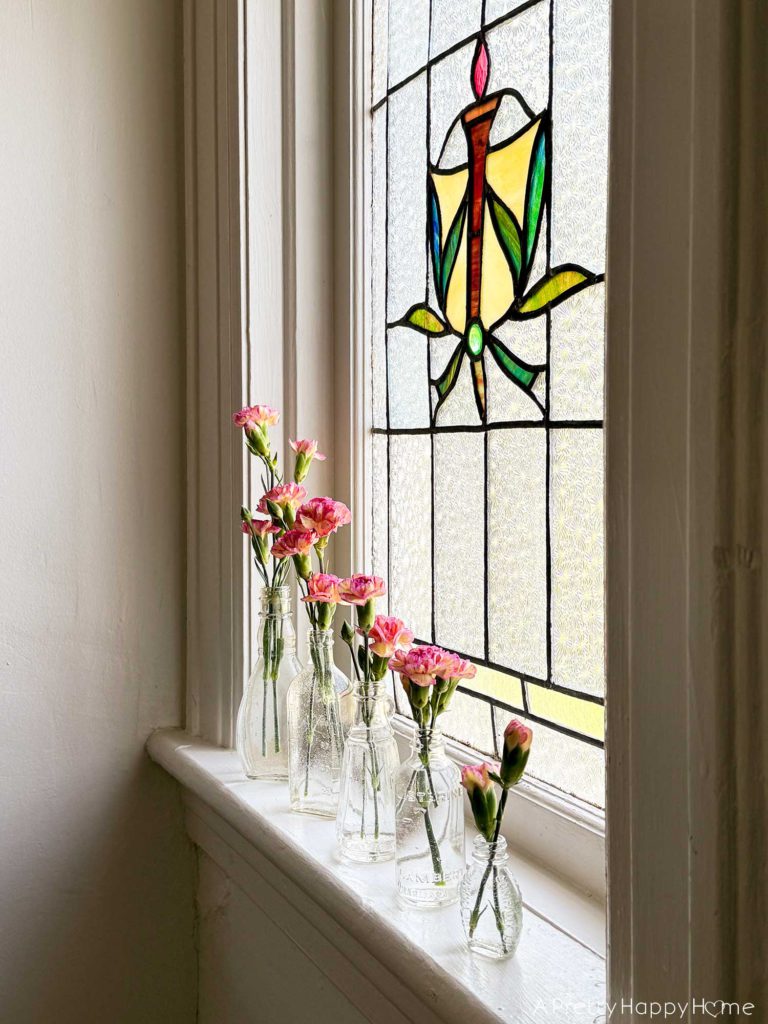 carnations in vintage bottle bud vases sitting on a stained glass window ledge