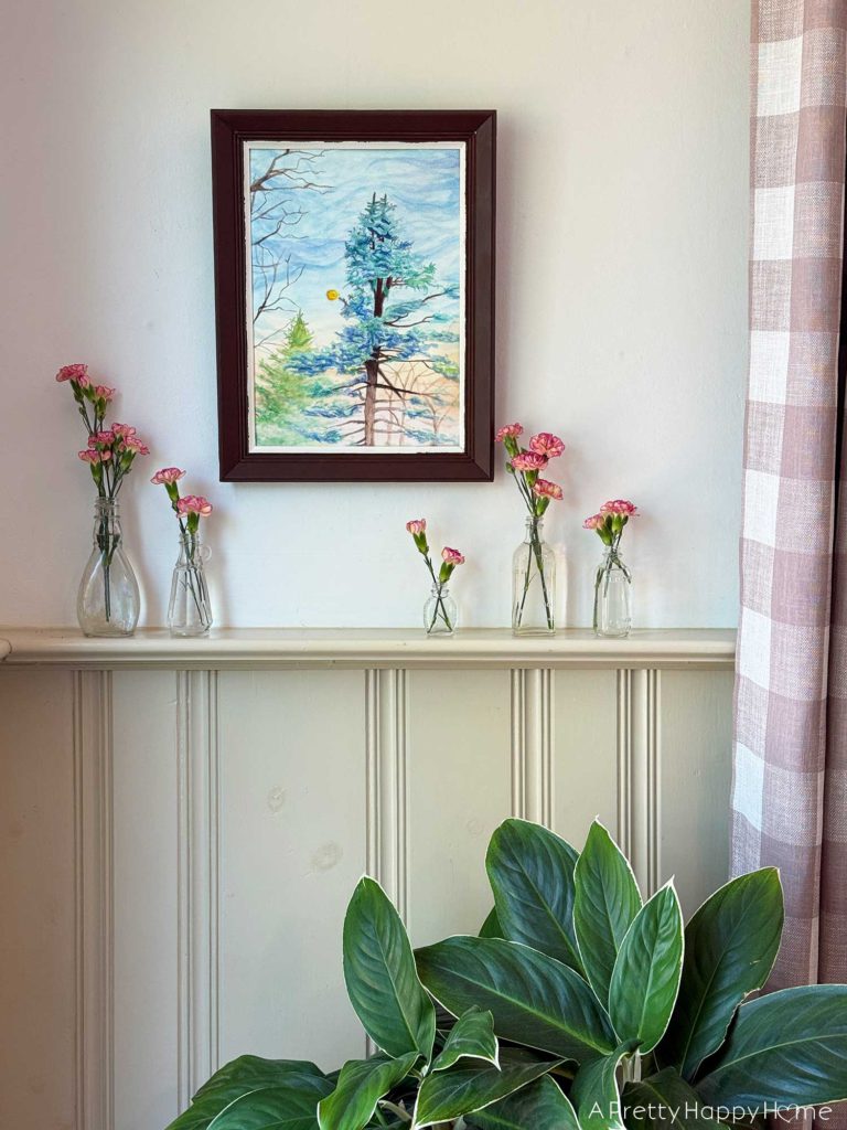 carnations in vintage bottle bud vases sitting on a ledge by a watercolor painting of a tree