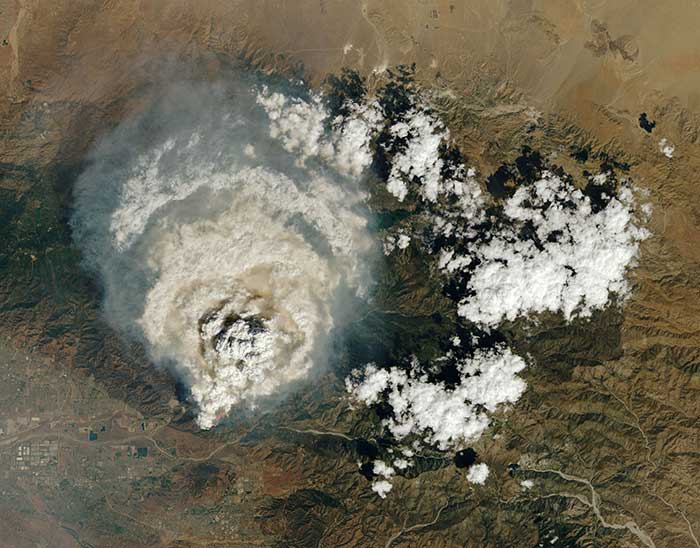 A pyrocumulus ("fire cloud") rising from the Line fire in Southern California. The image includes observations of shortwave-infrared light (red) to highlight the locations of active fires. A faint line of pink fire retardant is also visible on the hills near Redlands. Credit: NASA Earth Observatory image by Lauren Dauphin, using Landsat data from the U.S. Geological Survey via phys.org