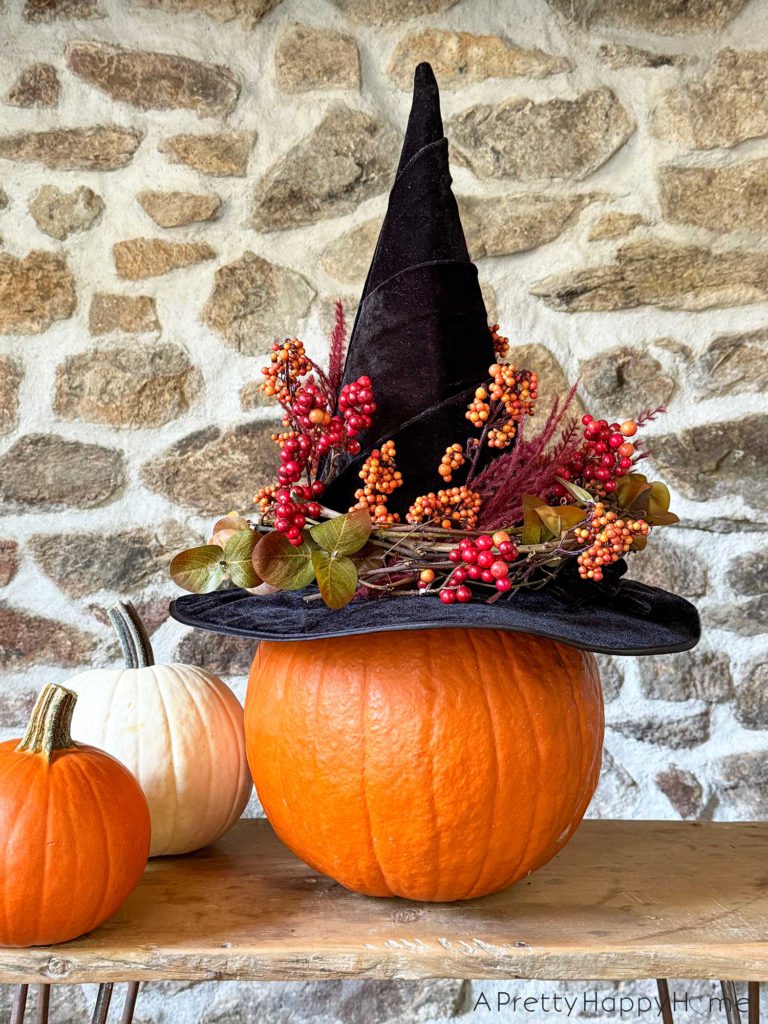 diy floral witch's hat sitting on a pumpkin in front of a stone wall