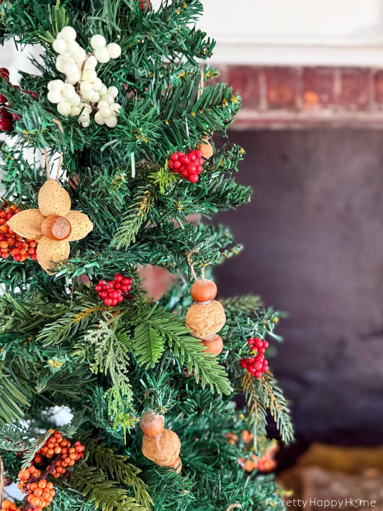 handmade nut ornaments using in-shell nuts how to decorate with nuts for Christmas christmas tree showing detail of ornaments made by hot glueing in-shell nuts together. Four almonds and one hazelnut can be hot glued together to make a flower. Two hazelnuts and a walnut can be glued together in a vertical stack. The handmade nut ornaments are hung by glueing a looped string to the back of the ornament. On the blog post five ways to decorate with nuts for christmas.