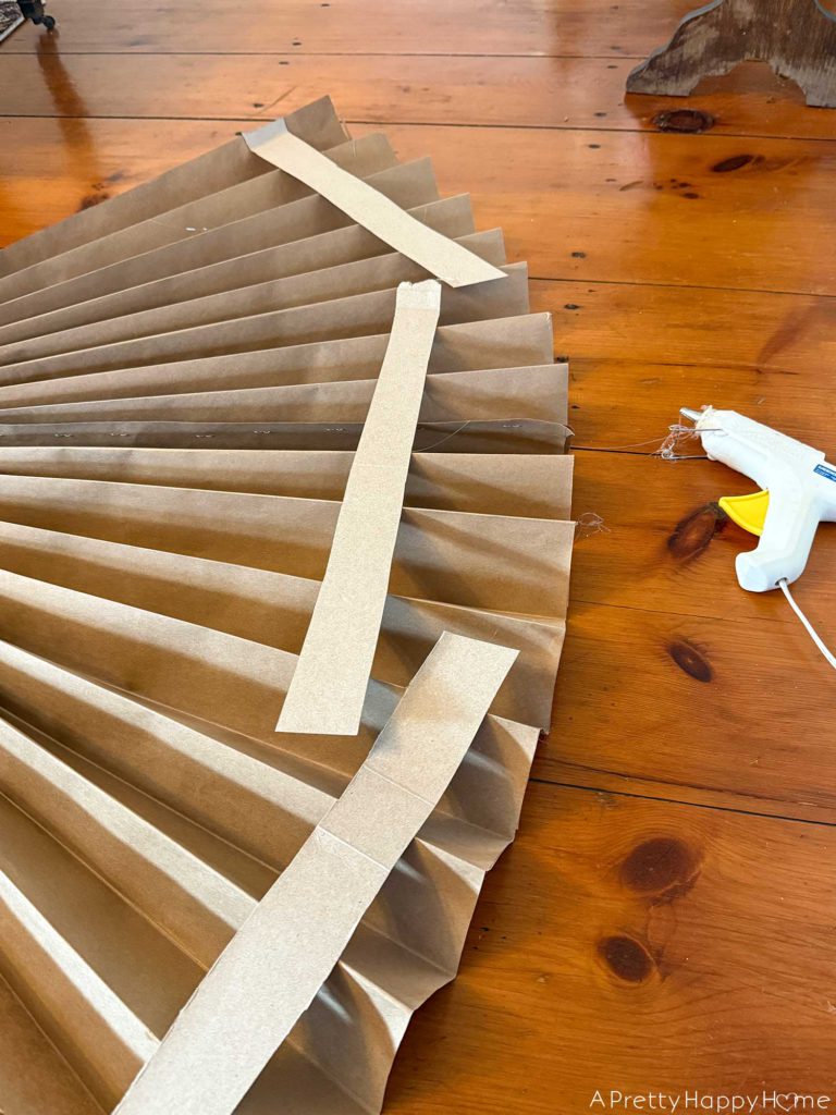 how to make a giant paper angel and keep the pleated skirt of the angel's dress fanned out by hot glueing thin strips of cardboard to the back of the dress