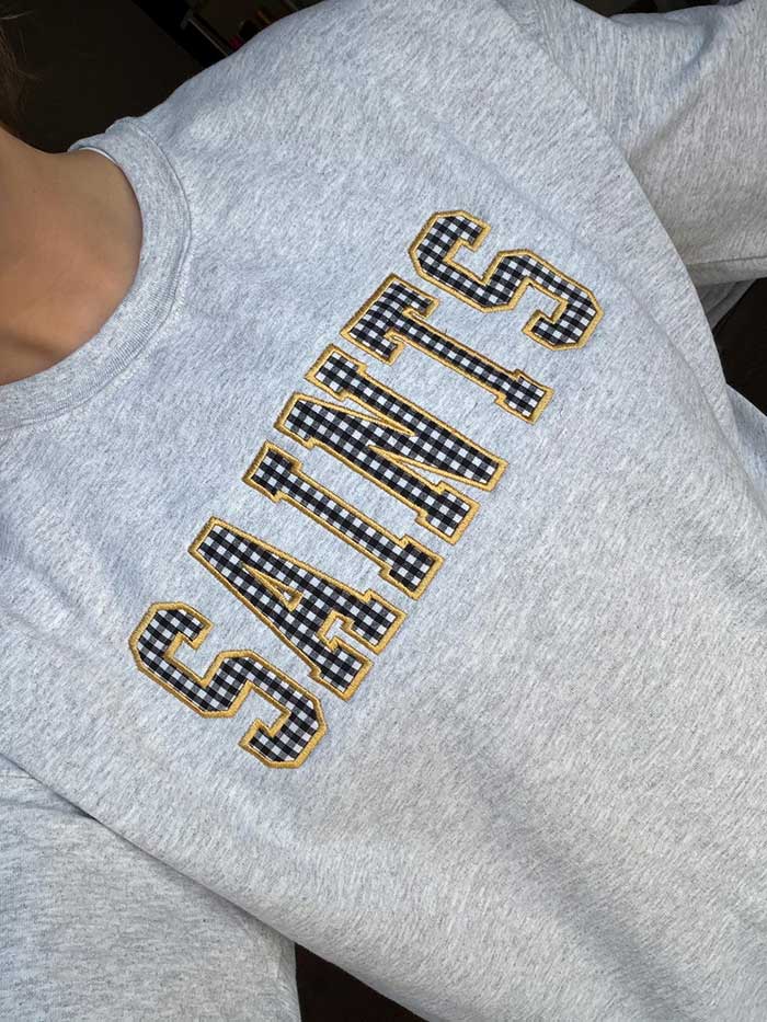 grey sweatshirt with custom gingham appliqué that says saints in black gingham fabric with yellow edge thread