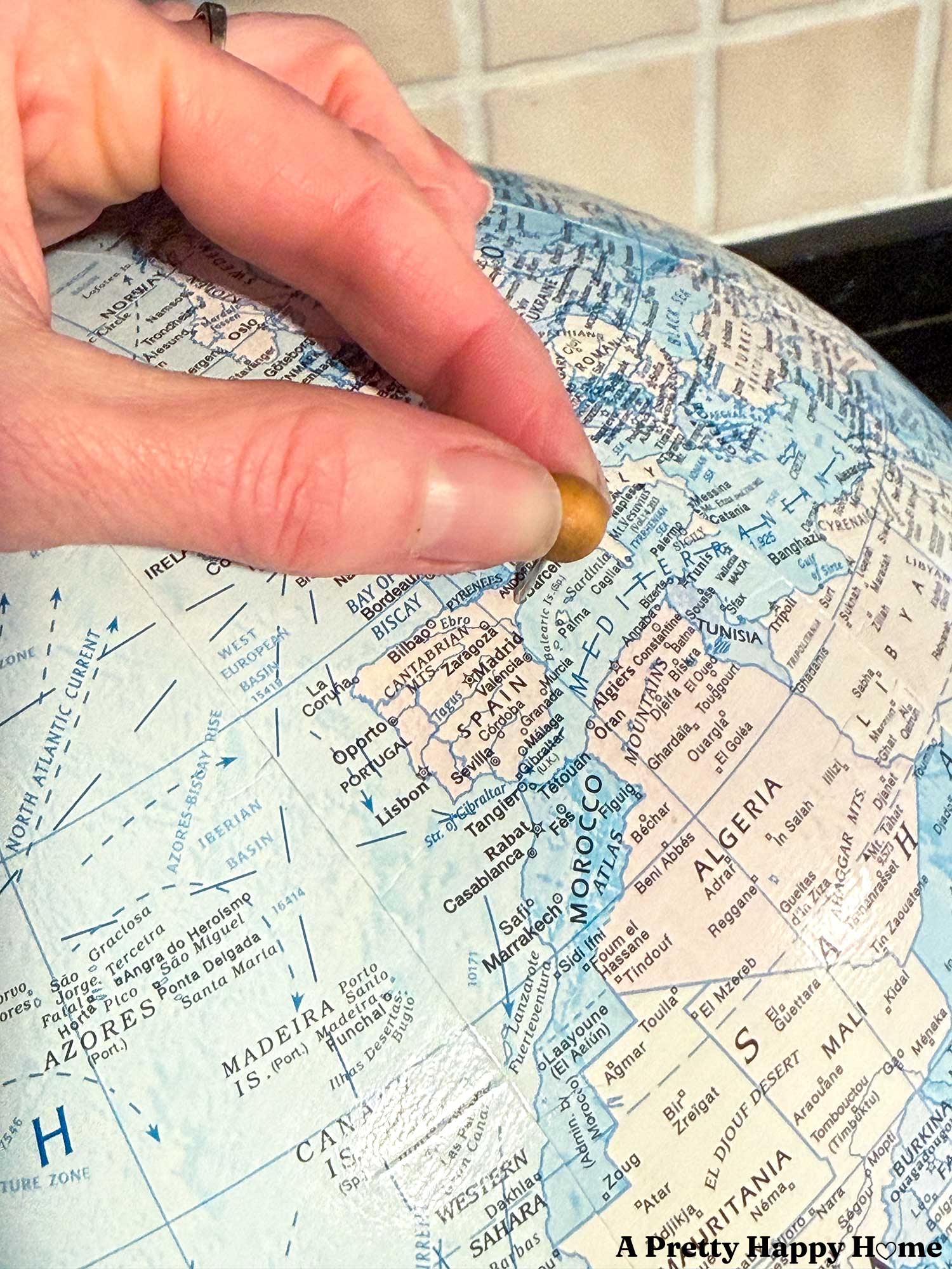 Hand pushing a wood push pin into a vintage globe to turn it into a diy push pin travel globe